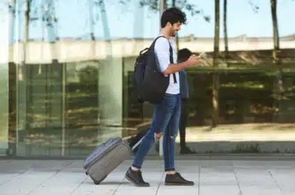 jovem carregando mala de viagem e mexendo no celular