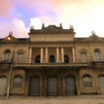 Fachada histórica do Theatro Guarany em Pelotas sob um céu de fim de tarde, destacando a arquitetura neoclássica e colunas frontais.