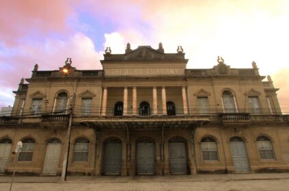 Fachada histórica do Theatro Guarany em Pelotas sob um céu de fim de tarde, destacando a arquitetura neoclássica e colunas frontais.