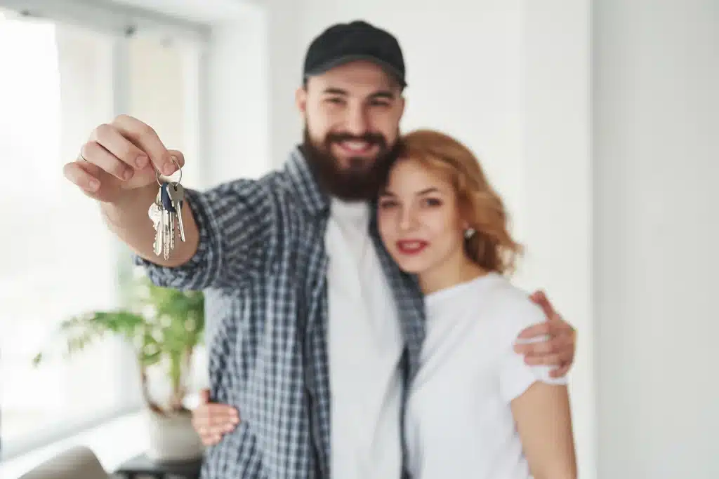 financiamento-imobiliario-casal-hetero-abracado-e-o-homem-segurando-uma-chave-na-mao