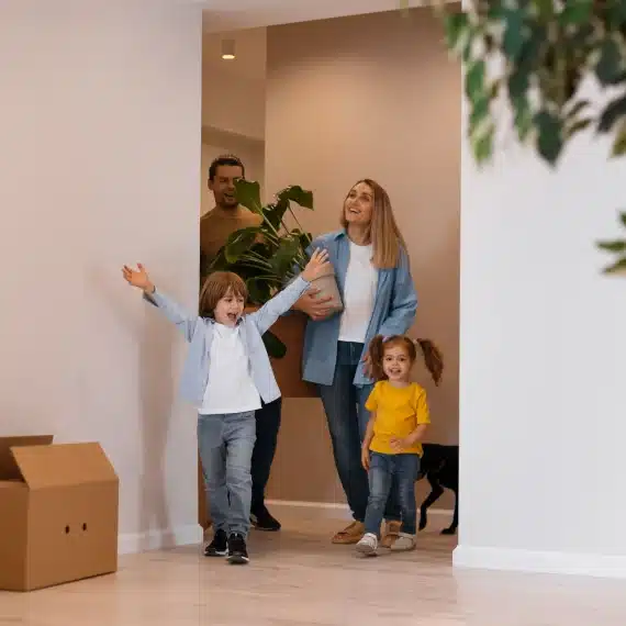 encontrar-o-imovel-ideal-familia-com-duas-criancas-entrando-na-nova-casa-com-uma-planta-nas-maos