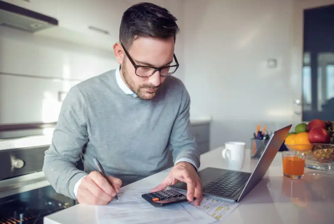 como-declarar-imposto-de-renda-de-aluguel-recebido-homem-sentado-na-cozinha-fazendo-calculos-na-calculadora