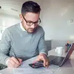 como-declarar-imposto-de-renda-de-aluguel-recebido-homem-sentado-na-cozinha-fazendo-calculos-na-calculadora