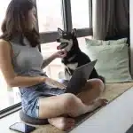 regras-para-animais-de-estimacao-em-condominio-mulher-jovem-sentada-na-janela-com-seu-cachorro-ao-lado