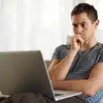 alugar-ou-comprar-imovel-homem-jovem-em-frente-ao-notebook-com-expressao-de-duvida