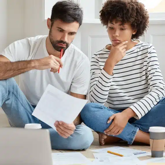 como-escolher-o-imovel-ideal-casal-sentado-no-chao-da-sala-analisando-papeis