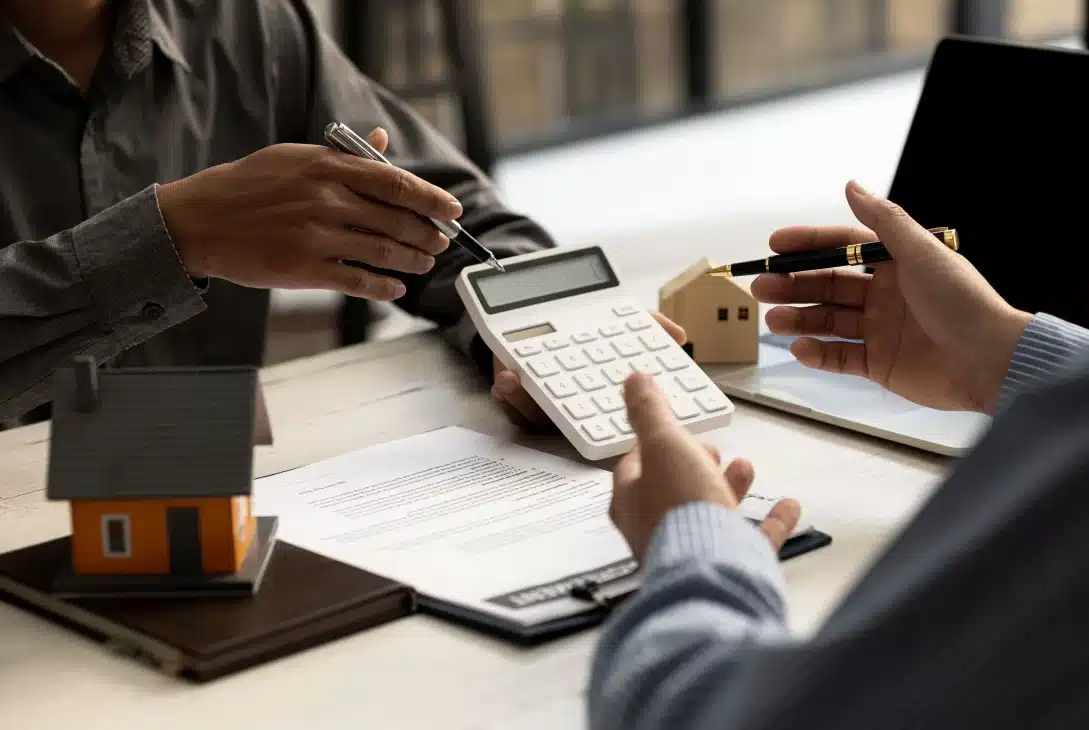 taxas-de-juros-de-financiamento-imobiliario-homens-conversando-sobre-uma-mesa-com-papeis-e-casas-em-miniatura