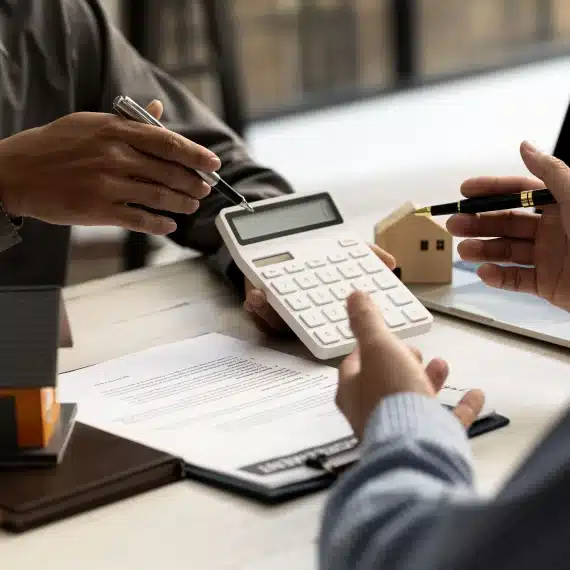 taxas-de-juros-de-financiamento-imobiliario-homens-conversando-sobre-uma-mesa-com-papeis-e-casas-em-miniatura