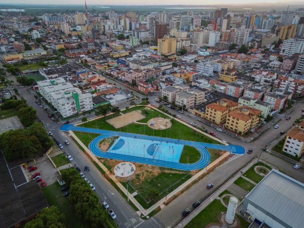 Vista da Praça Palestina em Pelotas após revitalização, mostrando pista de caminhada, quadra poliesportiva e área pet-friendly.