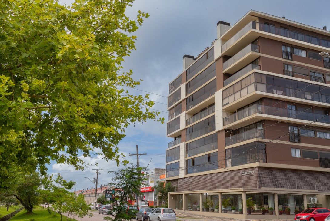 Prédio residencial moderno de fachada marrom com varandas envidraçadas, localizado em esquina arborizada.