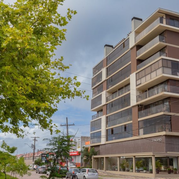 Prédio residencial moderno de fachada marrom com varandas envidraçadas, localizado em esquina arborizada.