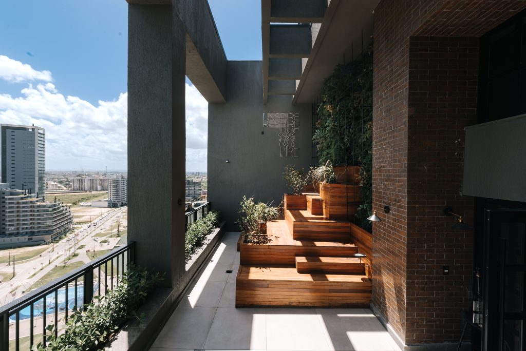 Área externa de cobertura com escada paisagística em madeira, vegetação vertical e vista para a cidade.