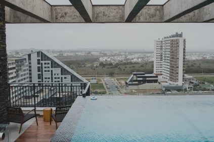 Vista panorâmica de condomínio moderno com piscina de borda infinita na cobertura e prédios residenciais ao fundo.