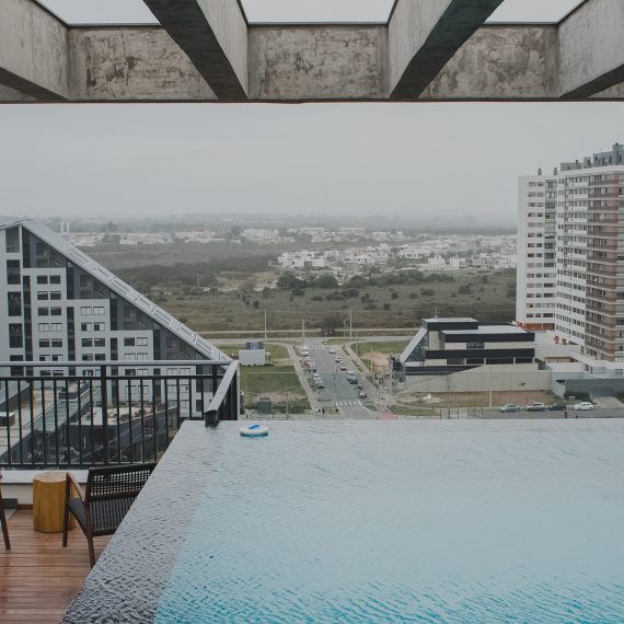 Vista panorâmica de condomínio moderno com piscina de borda infinita na cobertura e prédios residenciais ao fundo.