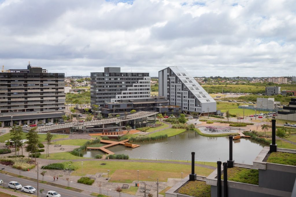 Vista aérea de bairro planejado com lago central, passarelas, áreas verdes e edifícios residenciais com design contemporâneo.