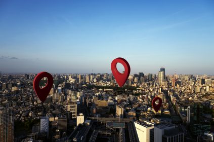 Ilustração com grandes marcadores vermelhos de localização sobrepostos a uma vista aérea de cidade, simbolizando pontos de interesse.