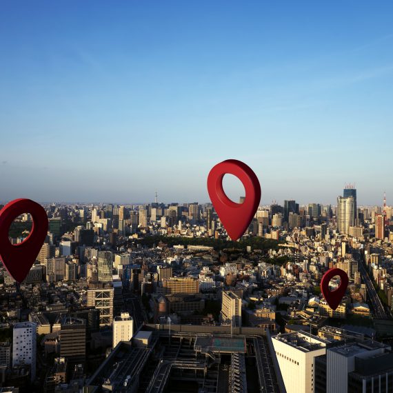 Ilustração com grandes marcadores vermelhos de localização sobrepostos a uma vista aérea de cidade, simbolizando pontos de interesse.