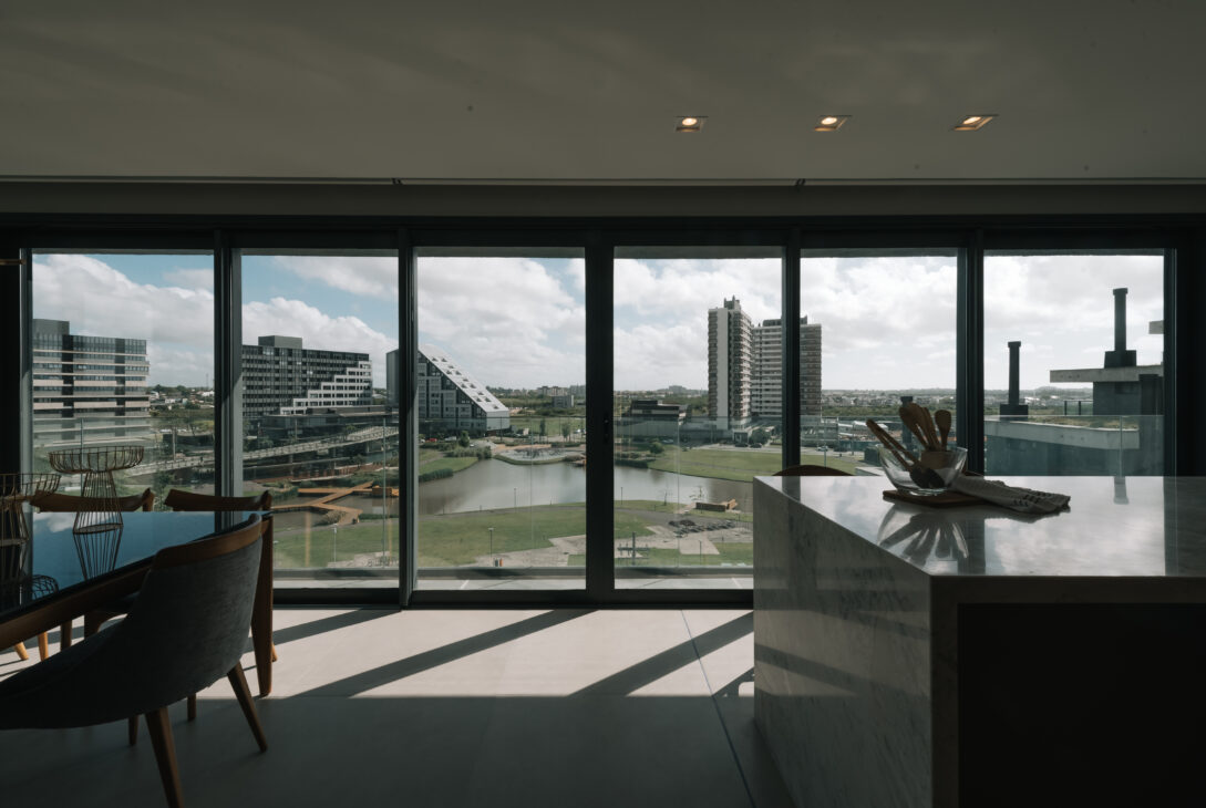 Sala integrada com grandes janelas de vidro e vista para prédios e área urbana.