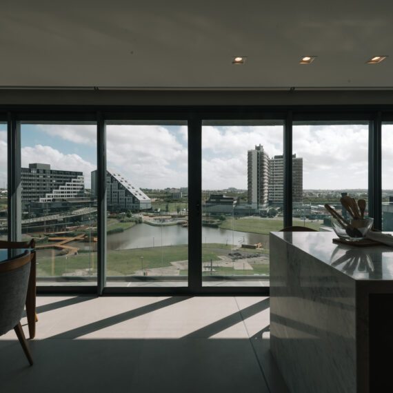 Sala integrada com grandes janelas de vidro e vista para prédios e área urbana.